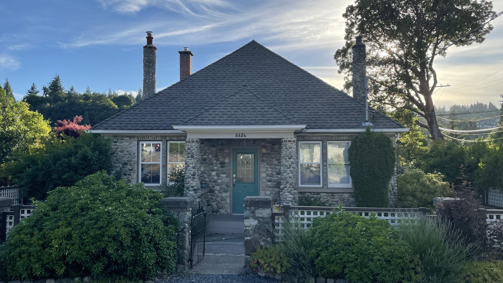 Charming stone cottage with a green door, surrounded by lush greenery and under a blue sky with wispy clouds.