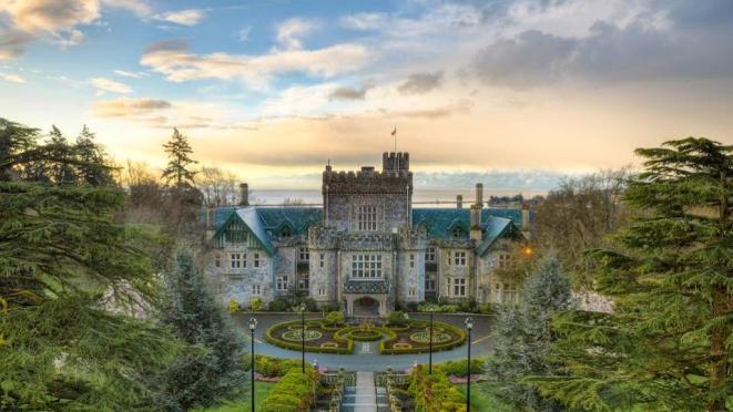 Grand historic Hatley castle with manicured gardens, surrounded by lush greenery and a dramatic sky in the background.