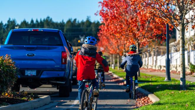 kids riding bikes on road by cars trees