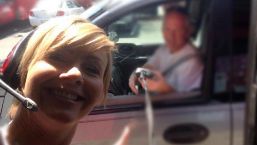 Selfie of woman with a person inside their car in the background. The background is blurry. 