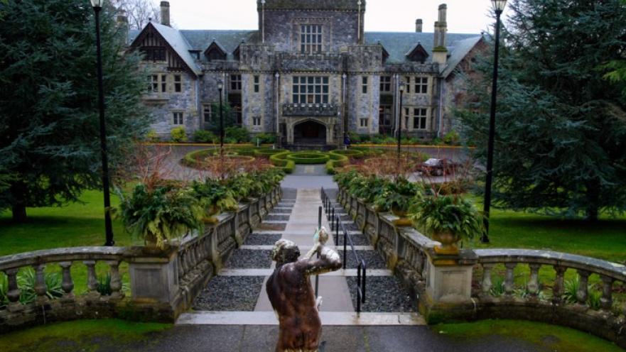 Entrance to hatley Castle. There is a statue in the foreground and a large rectangular stone castle in the background.