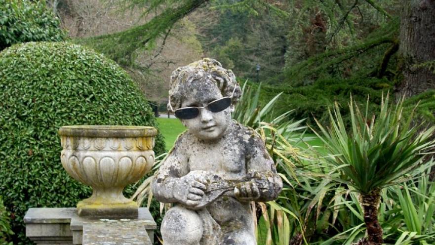 Angel statuette with dark sunglasses on. The angel is also holding a lute.