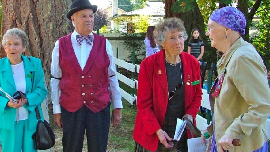 Group of elderly people talking with each other. The group is all standing outside.