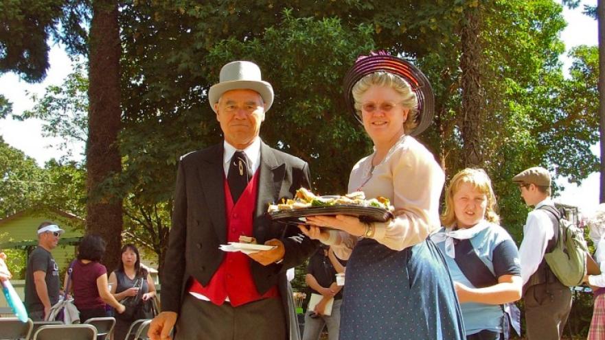 Man and woman wearing old-timey clothes. The woman is holding a tray with cookies.