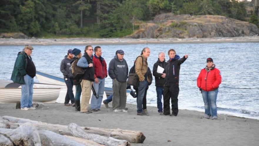 Film production crew on beach. There is a group of people on the beach with one among the group giving directions to the rest.