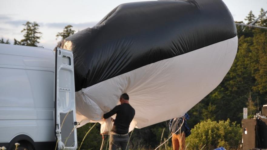 Film crew unloading large, inflatable light reflector from truck.