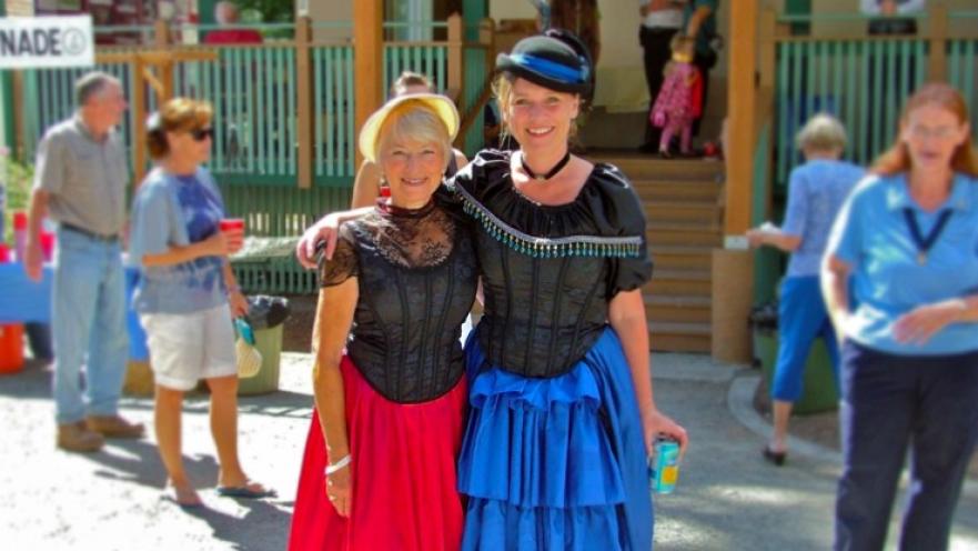 Two smiling women wearing old-timey clothes.