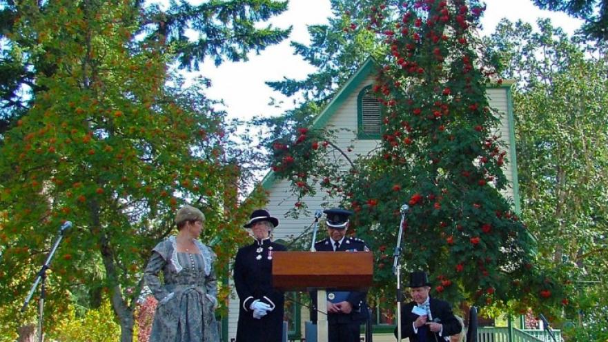 Group of people standing in front of an old church building. There is a podium and stage in front of the church.