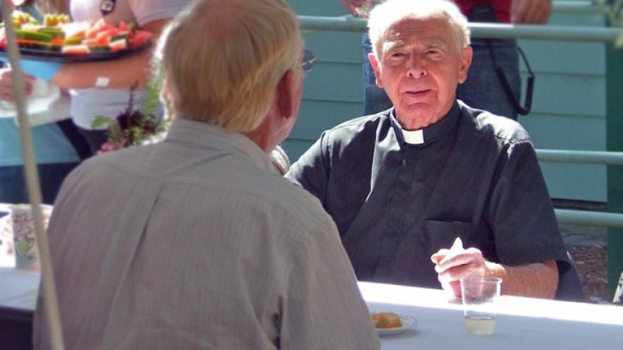 Elderly reverend sitting across from an elderly man.