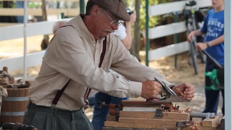 Man dressed in old-timey clothes. The subject is doing woodwork.