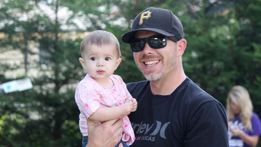 Man wearing dark sunglasses carrying a child. The man is smiling.