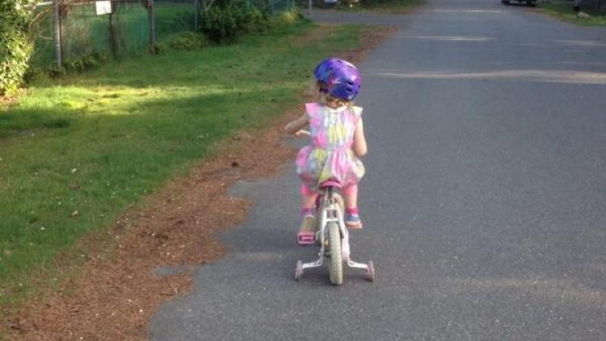 Girl riding bicycle down a road. The girl is wearing a purple bicycle helmet.