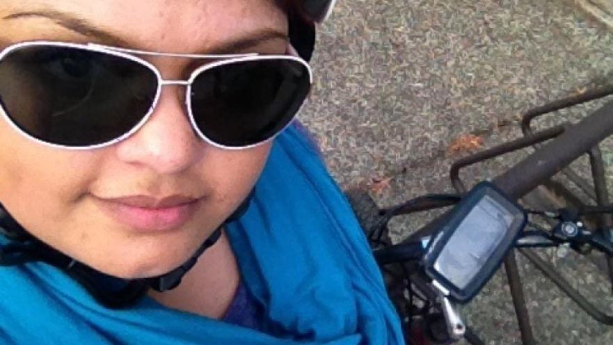 Selfie of girl wearing dark sunglasses and a bicycle helmet. The subject is standing next to their bicycle.