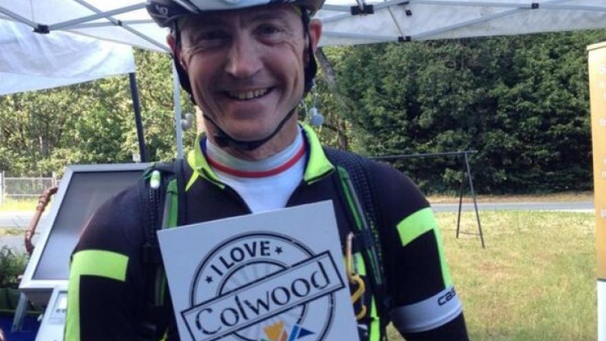 Selfie of man wearing bicycle gear. The subject is holding a sign that reads "I love Colwood."