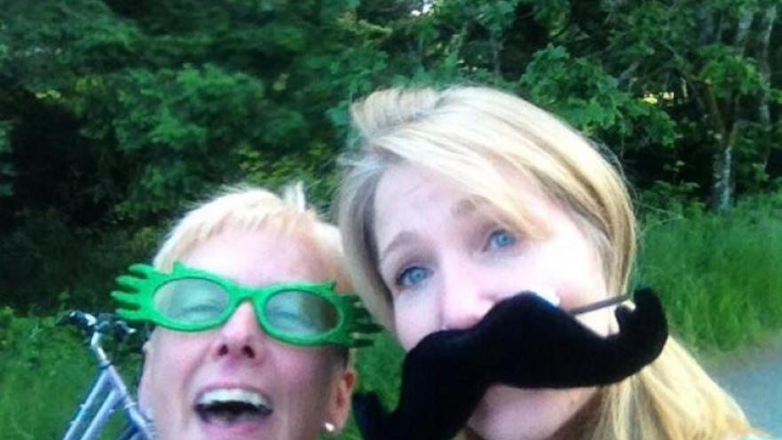 Selfie of two women. One subject is wearing green novelty glasses while the other is wearing an oversized novelty moustache. 