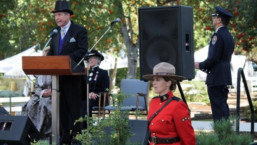 Man wearing a top hat giving a speech at a podium. There is a mountie in the foreground. 