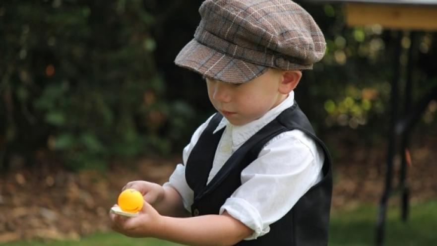 Child playing with an egg on spoon toy. The child is wearing a hat.