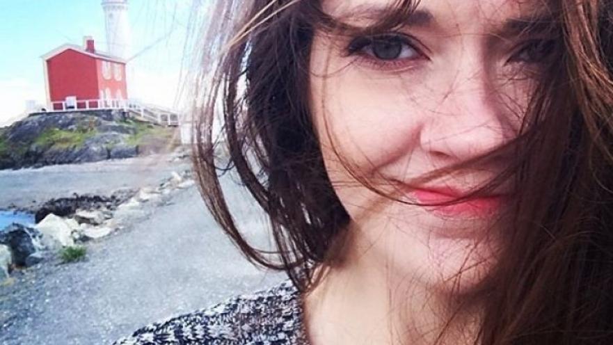 Selfie of woman with long brown hair. There is a lighthouse in the background.