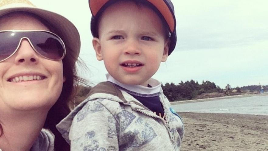 Selfie of mother with her child. The woman is wearing sunglasses while the child has an orange baseball cap. The subjects are at a beach.