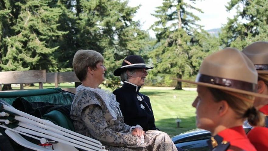 Two older women riding on a horse-drawn carriage. There are some mounties in the foreground.