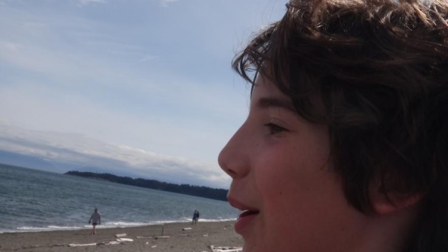 Child with unkempt hair standing on beach.