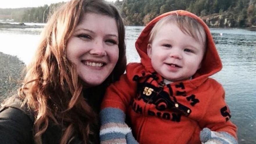 Woman and child near a body of water. The child is wearing an orange hoodie and some mittens.