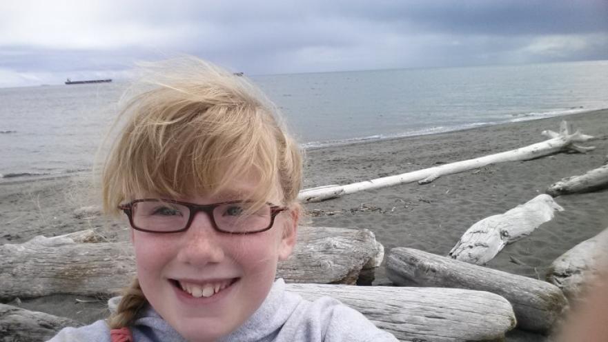 Selfie of smiling girl with glasses at a beach.