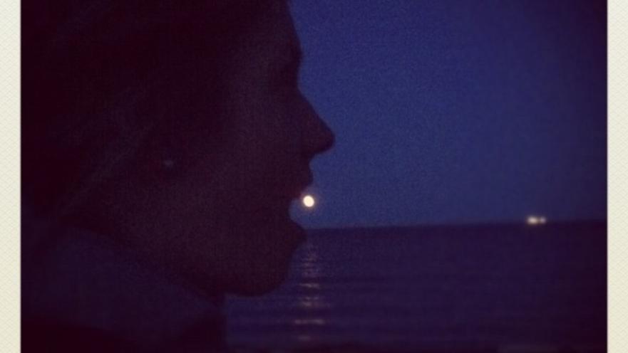 Dark image of person pretending to eat the moon in the background.