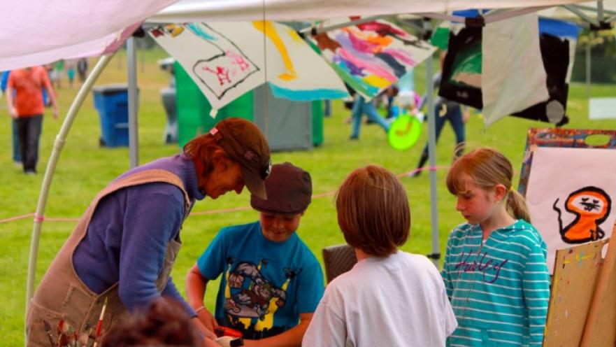 Children huddled around a woman teaching them painting. 