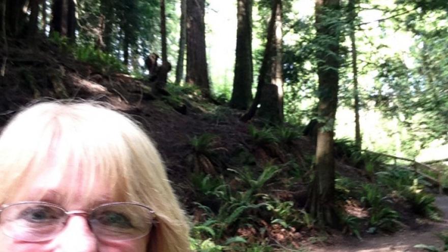 Selfie of smiling blonde woman with glasses in the middle of a forest.