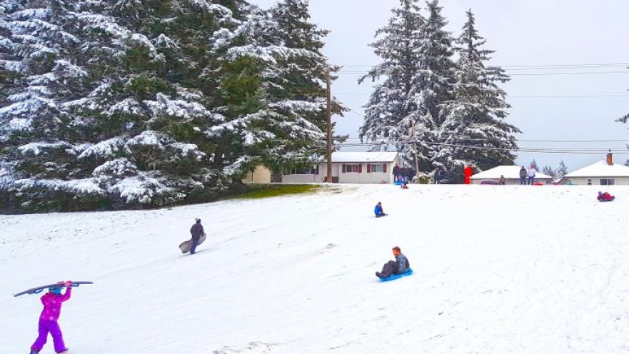 People enjoying and playing in the snow. The ground is completely covered in snow.