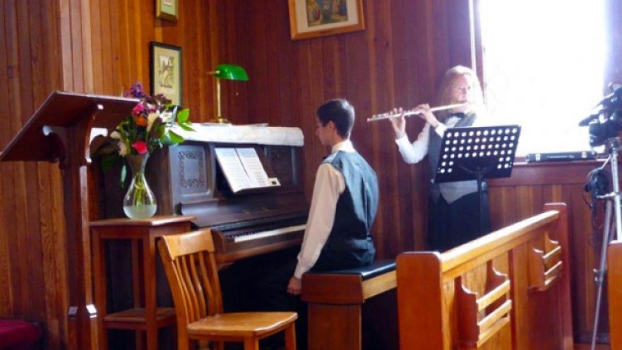 Piano and flute musicians playing their instruments inside a church.