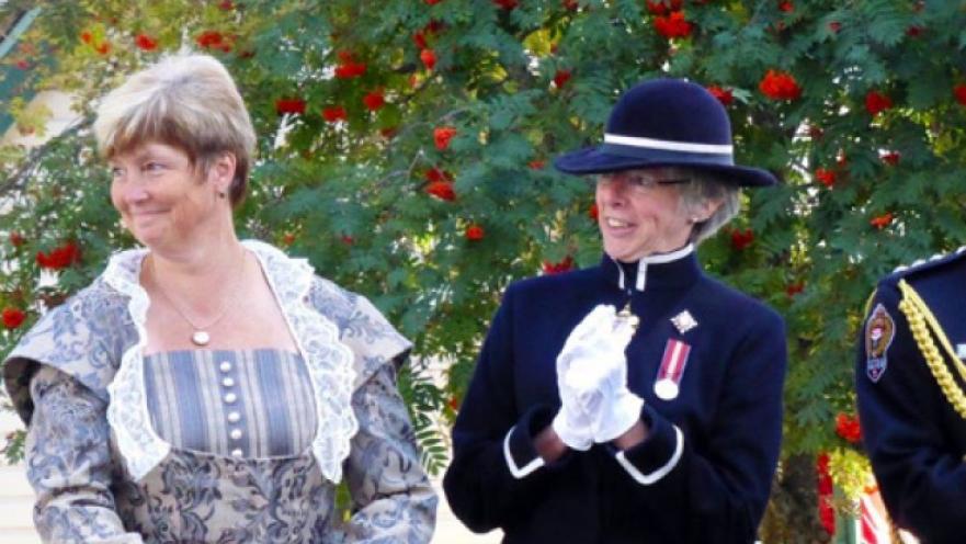 Tow women dressed in old-timey clothes smiling and looking to the side.