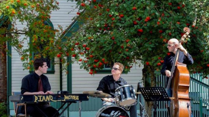 Three piece band playing music at a stage.