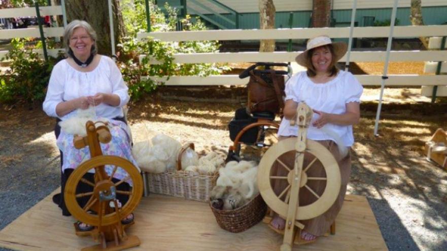 Two women smiling as they spin wool into yarn.