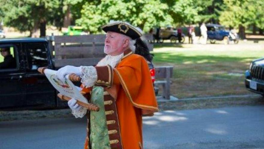 Person dressed as an old-timey town crier. The subject is reading off from a scroll.