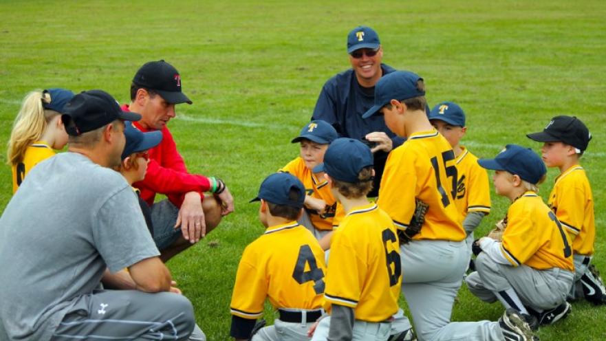 Little league baseball team with coaches. The team is huddled up and the coach is speaking to the team.