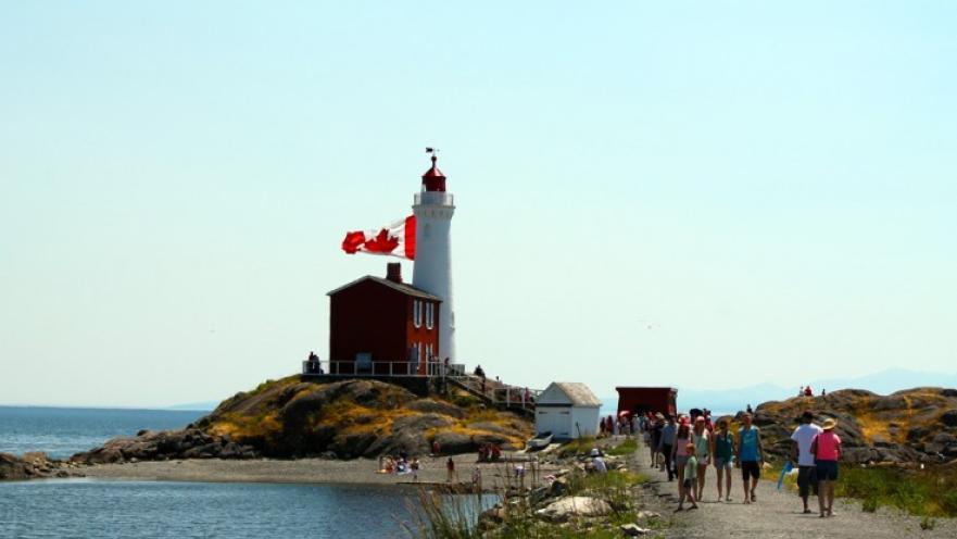 Red and white lighthouse. There is a large Canada flag flying on a flagpole.