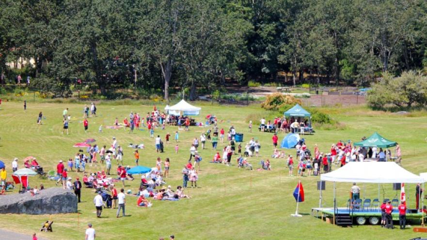 Crowd celebrating Canada day. There are some tents on a large field.