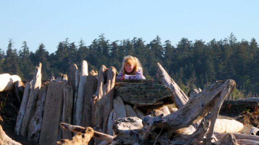 Girl peeking out from a pile of driftwood.