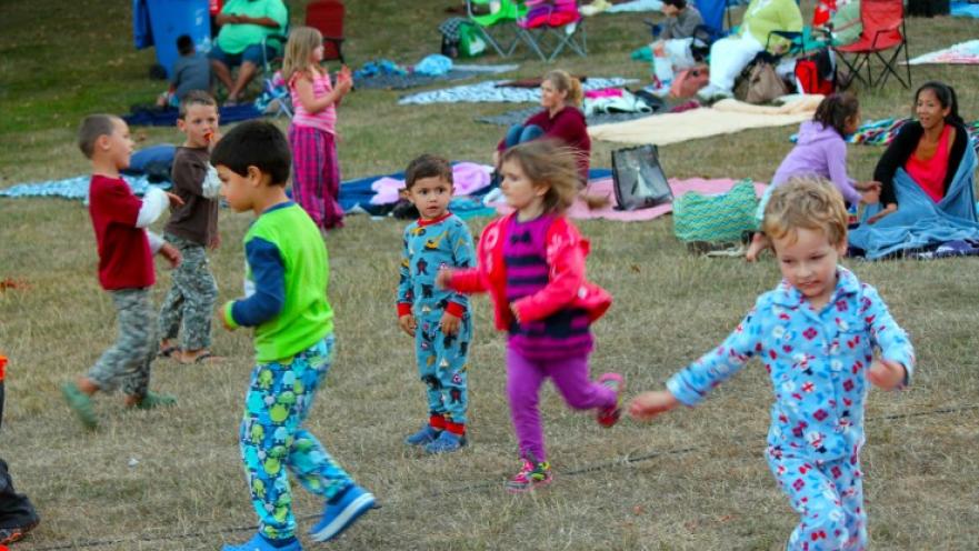 Children dressed in brightly coloured pyjamas dancing and playing in a field.