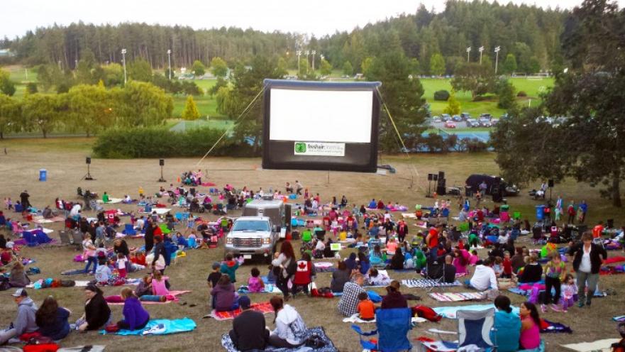 Crowd gathered watching a movie on a large inflatable screen.