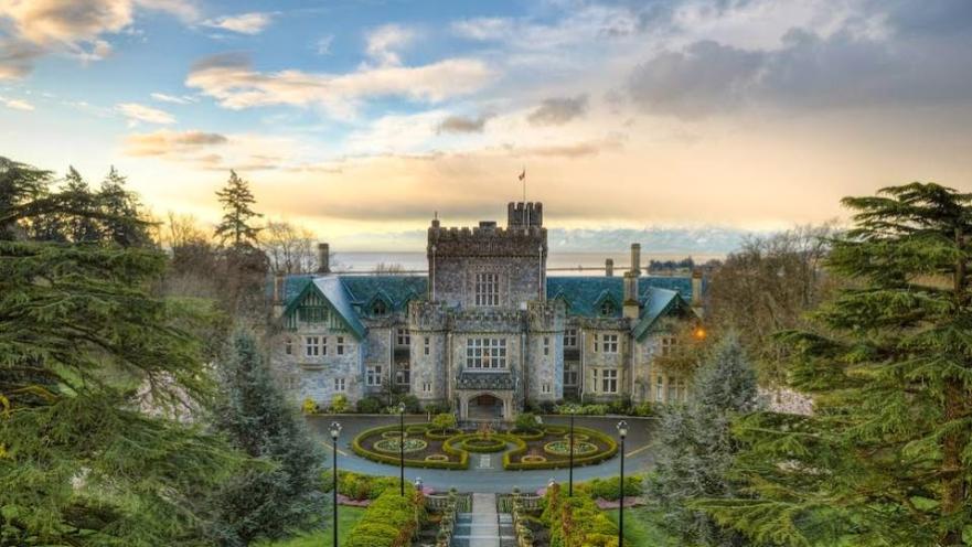 Grand historic Hatley castle with manicured gardens, surrounded by lush greenery and a dramatic sky in the background.