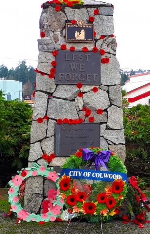 A memorial stone monument adorned with red poppies and a wreath that reads "City of Colwood," commemorating fallen soldiers with the inscription "Lest We Forget."