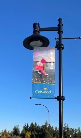 Streetlight banner in Colwood with an image of a child in a pink coat and red hat, labeled "thoughtful."