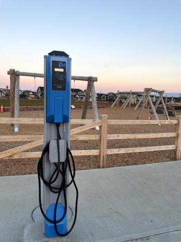 Electric vehicle charging station with a playground in the background, captured during dusk.