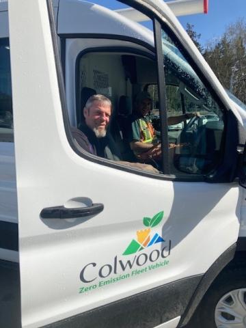 Two utility workers sitting inside a Colwood Zero Emission Fleet Vehicle, smiling at the camera.