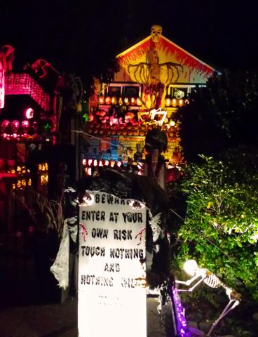 Spooky Halloween house decorated with skeletons, pumpkins, and a "Beware" sign.