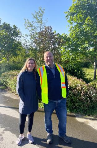 Two people smiling and posing on a sunny day, one wearing a reflective safety vest.