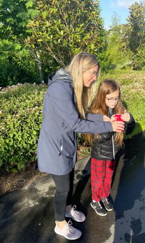 An adult and child observing something in a red cup in a park, surrounded by greenery.